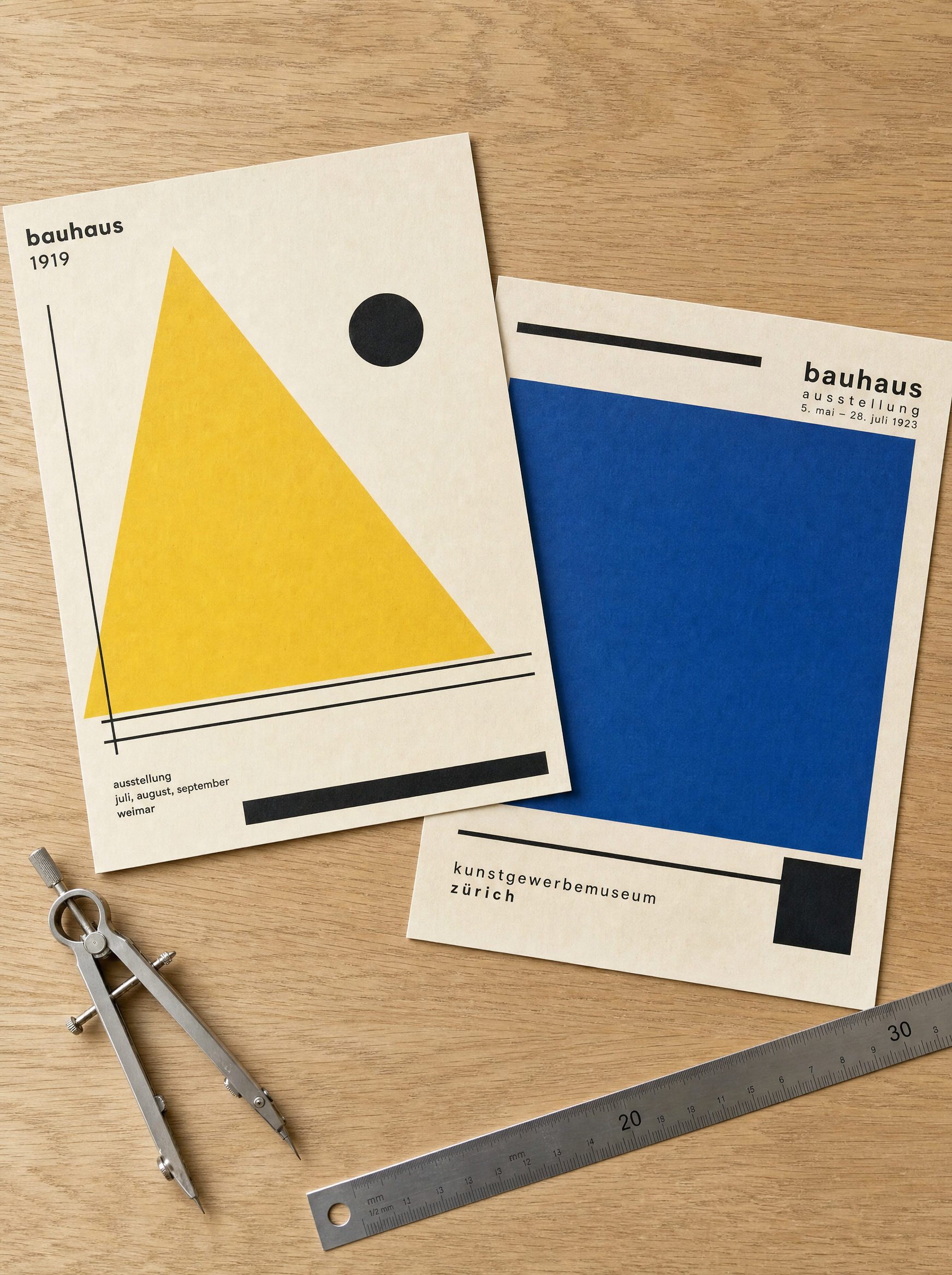 Two Bauhaus art prints with geometric triangle and rectangle motifs arranged on a light oak desk