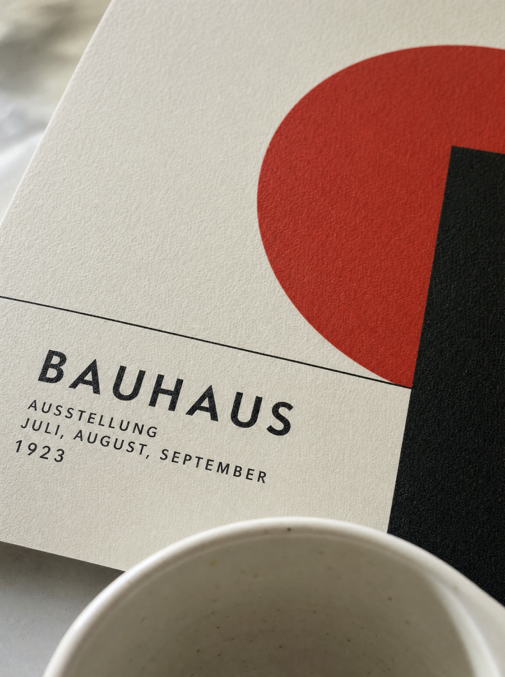Close-up detail of a Bauhaus print surface showing ink texture on heavyweight matte art paper with a white ceramic cup