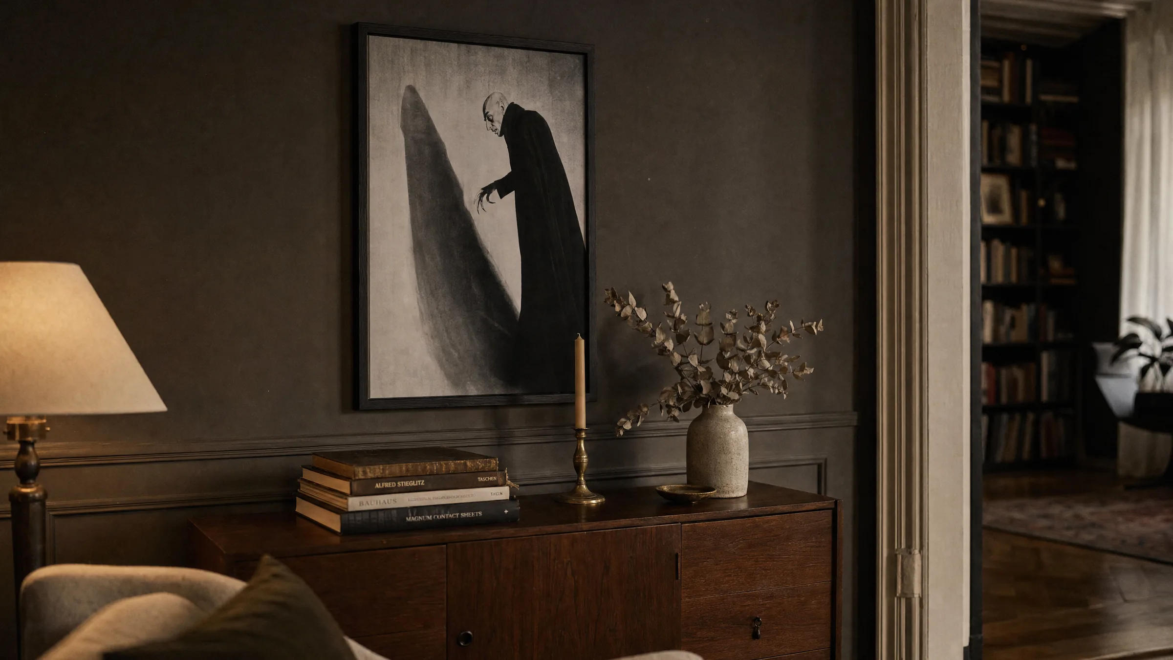 Nosferatu poster in a slim black frame above a dark wooden sideboard with a candle and books