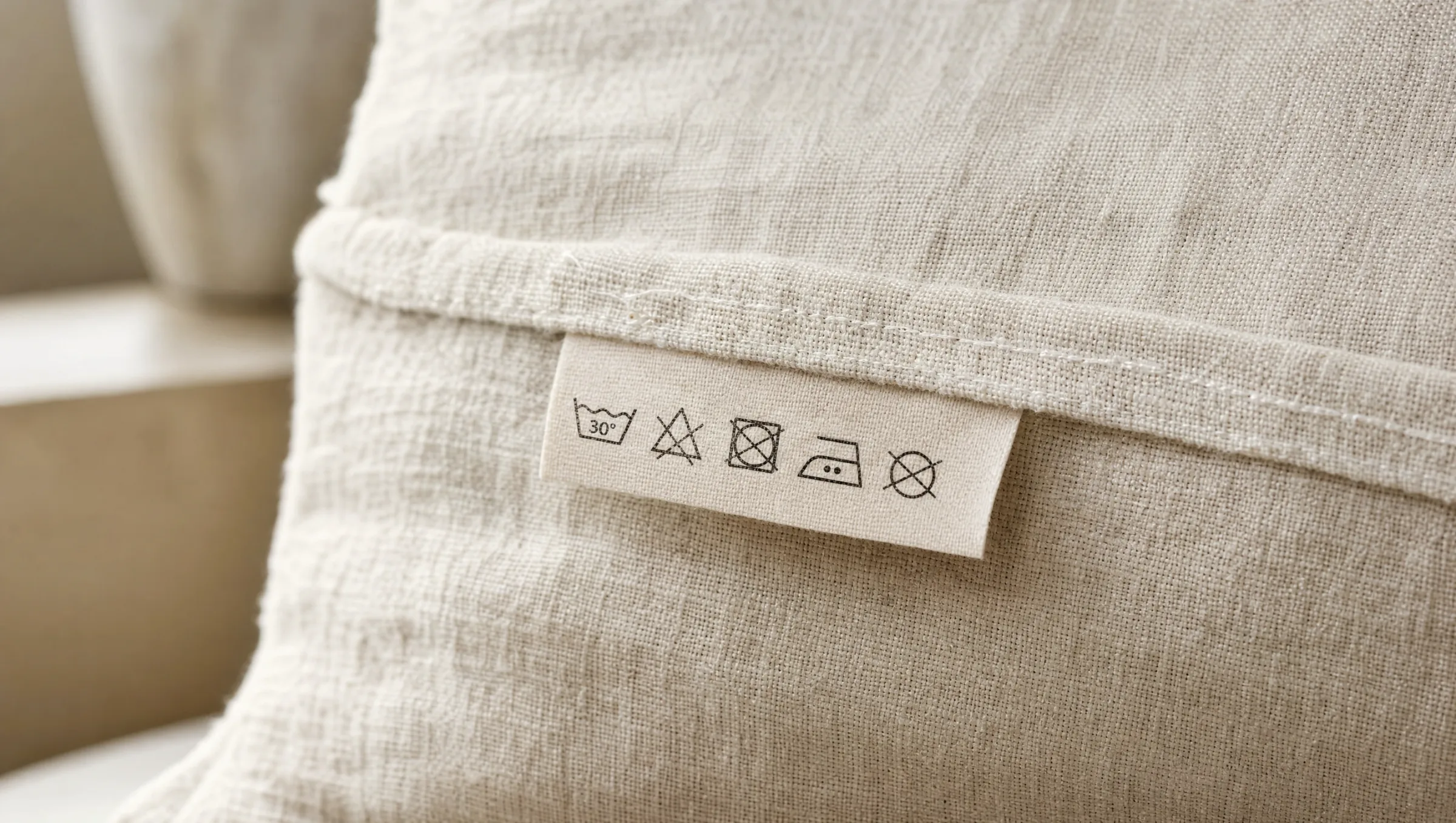 Close-up of a textile care label on a natural linen fabric showing laundry care symbols